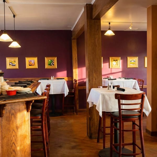 Warm restaurant dining room with high tables, a bar, and a wine rack against plum walls.