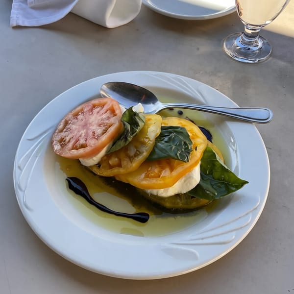 A white plate holds a colorful Caprese salad with red and yellow tomatoes, mozzarella, and basil.