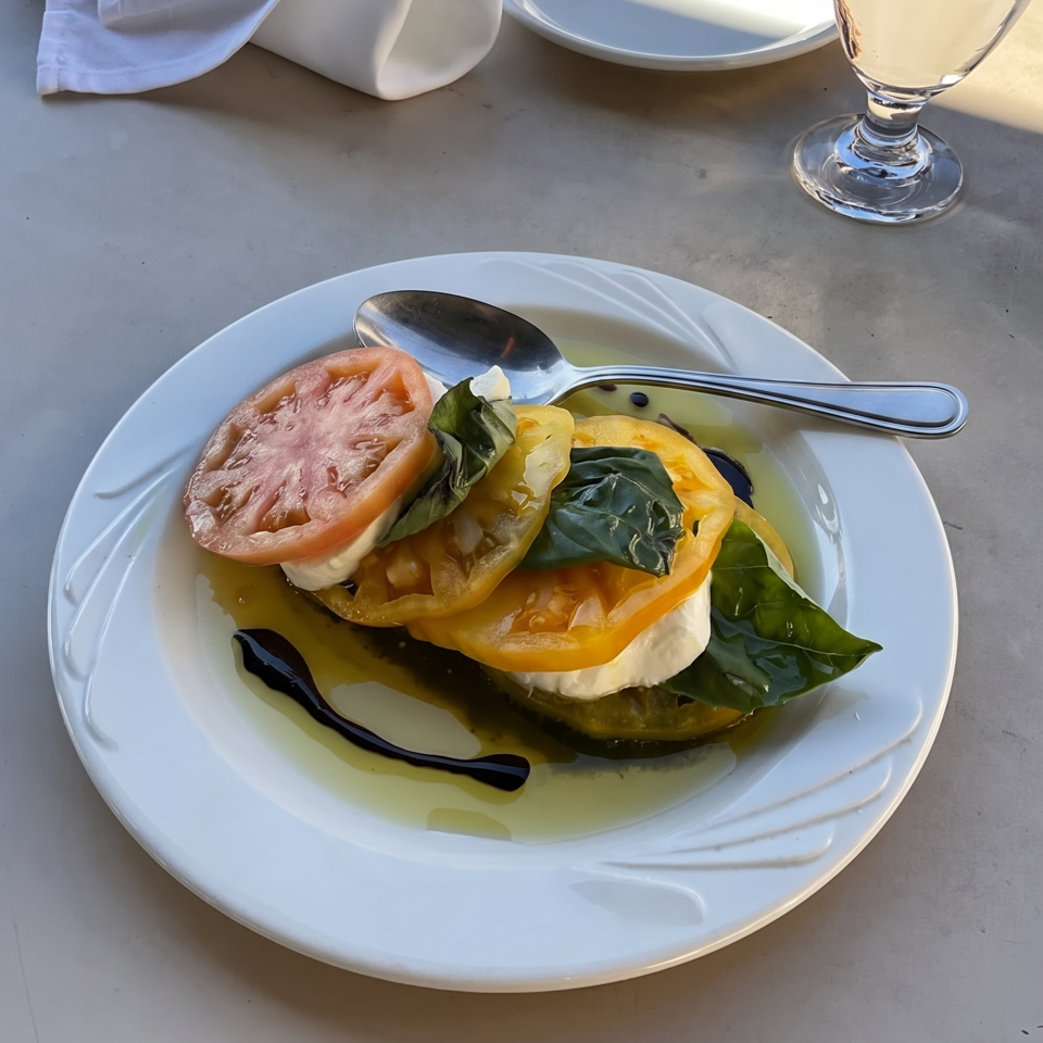 A white plate holds a colorful Caprese salad with red and yellow tomatoes, mozzarella, and basil.