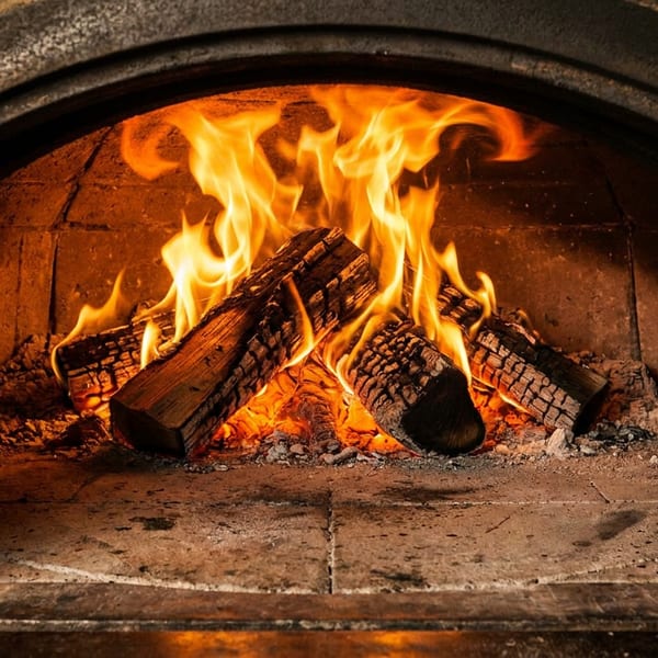 Burning logs and bright orange flames inside a traditional wood-fired oven.