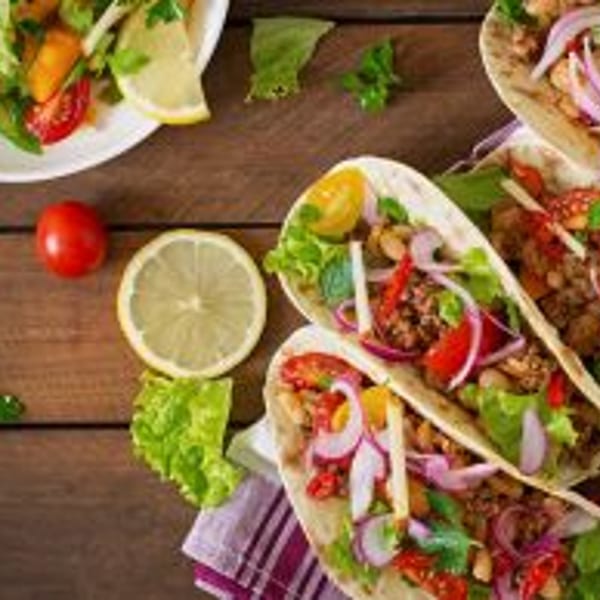 Four vibrant tacos and a fresh green salad on a rustic wooden table.